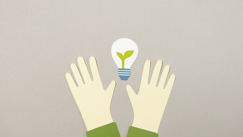 Illustrative paper cutouts featuring hands and a light bulb with a plant, symbolizing environmental awareness.